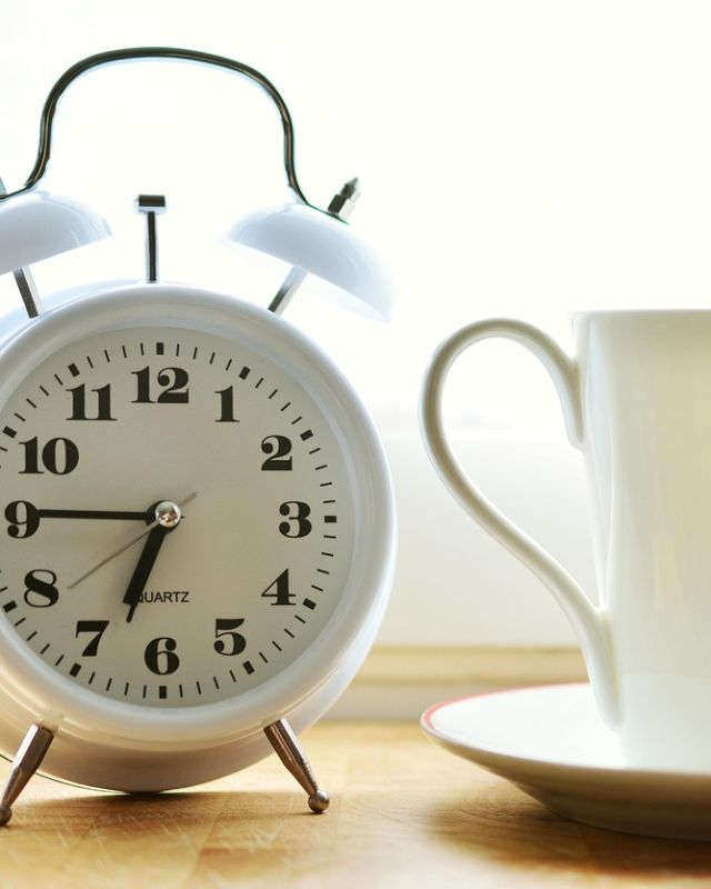 An alarm clock and a cup of coffee on a sunny windowsill