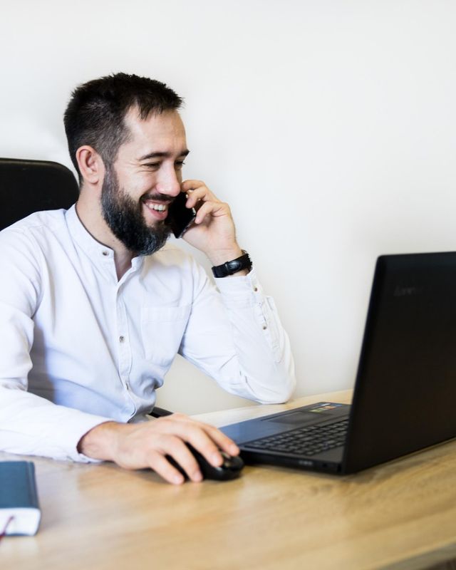 A man smiling on a phone call at his desk