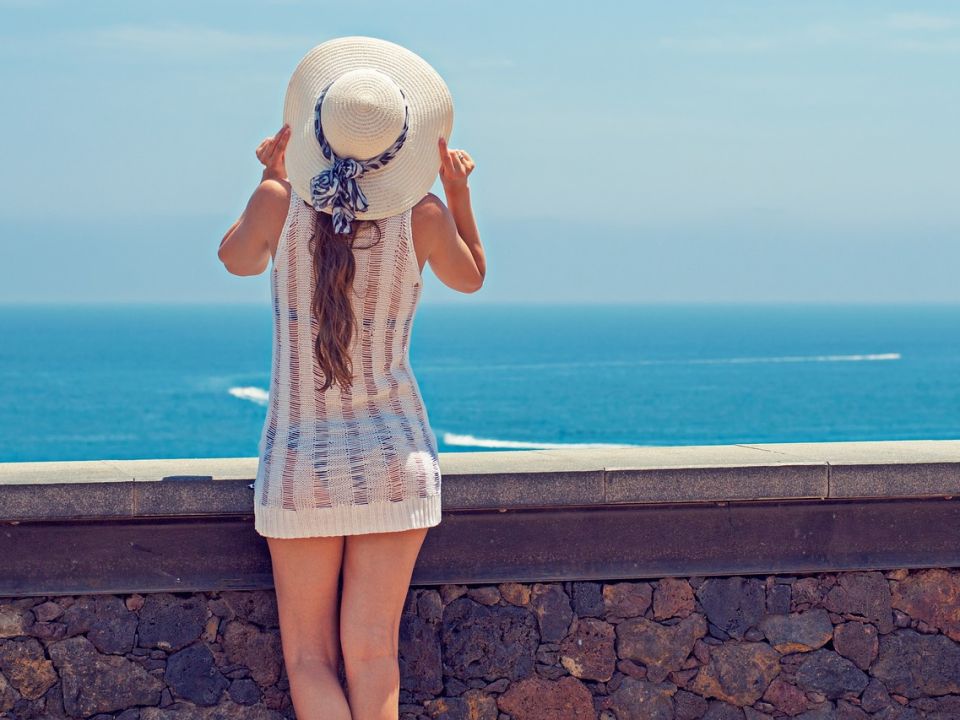 A woman in a sun hat looking out at the ocean